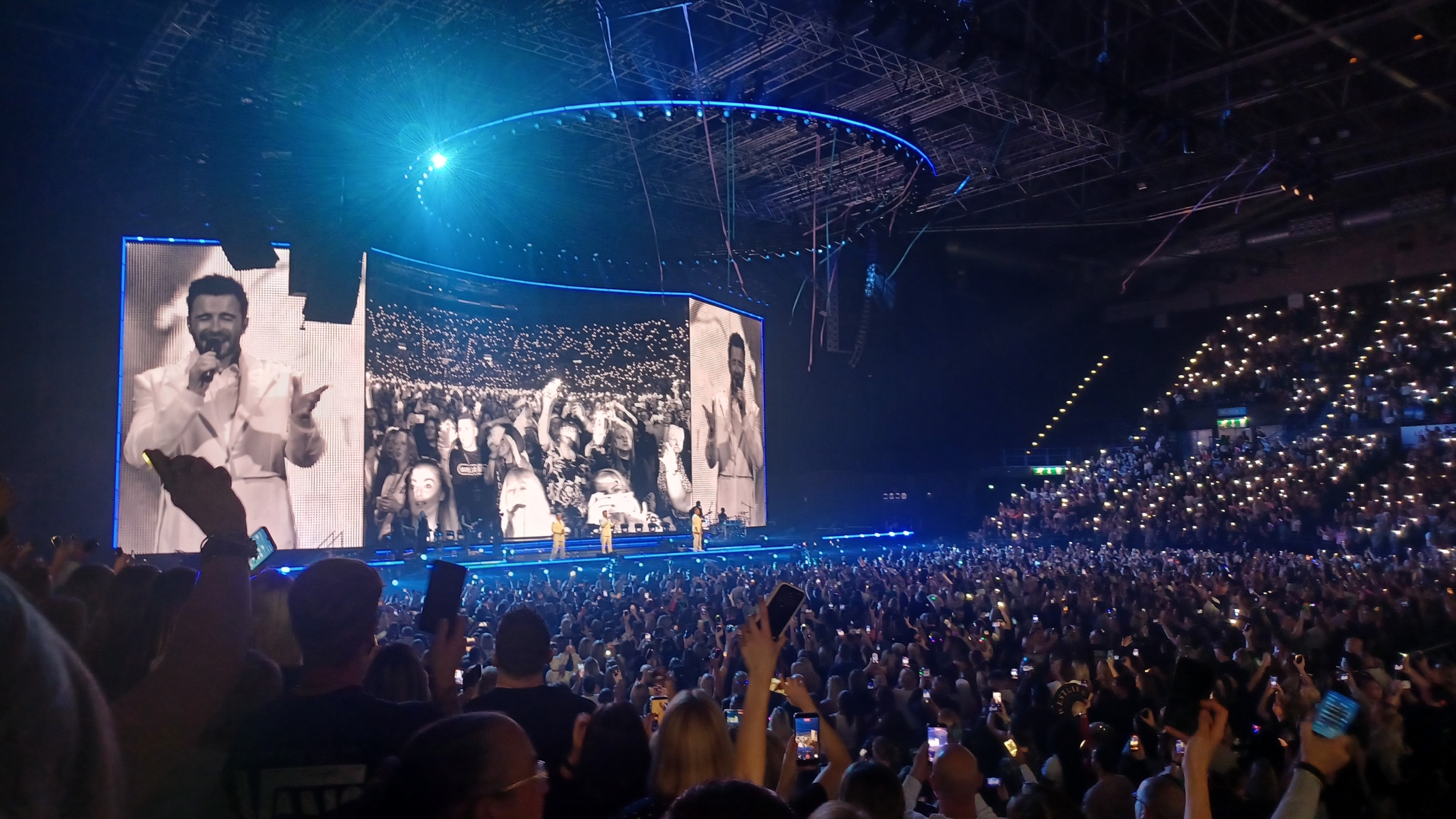 Westlife performing at Utilita Arena Birmingham, with large stage screens and the audience in view
